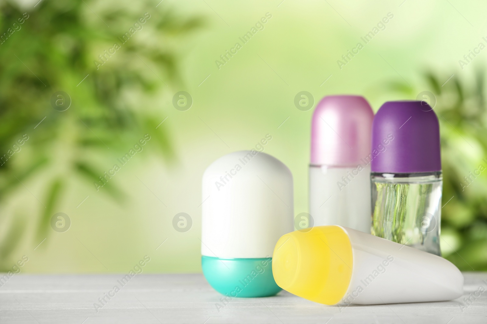 Photo of Different deodorants on white wooden table against blurred background. Space for text