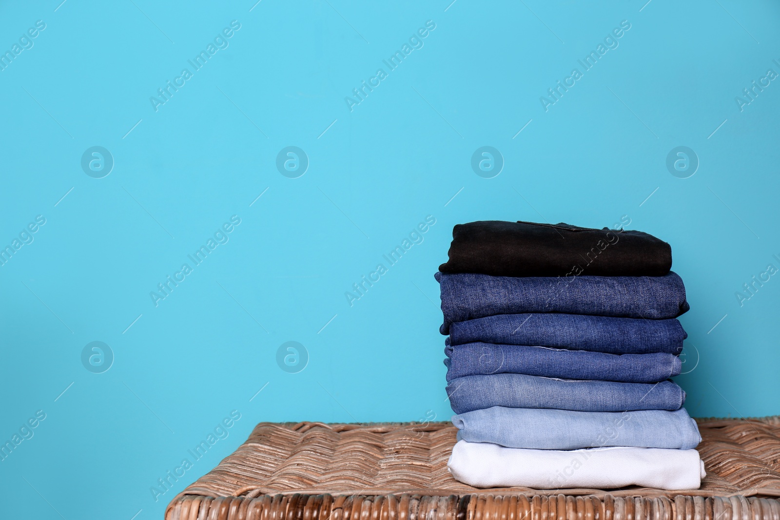 Photo of Stack of different jeans on basket against color wall with space for text