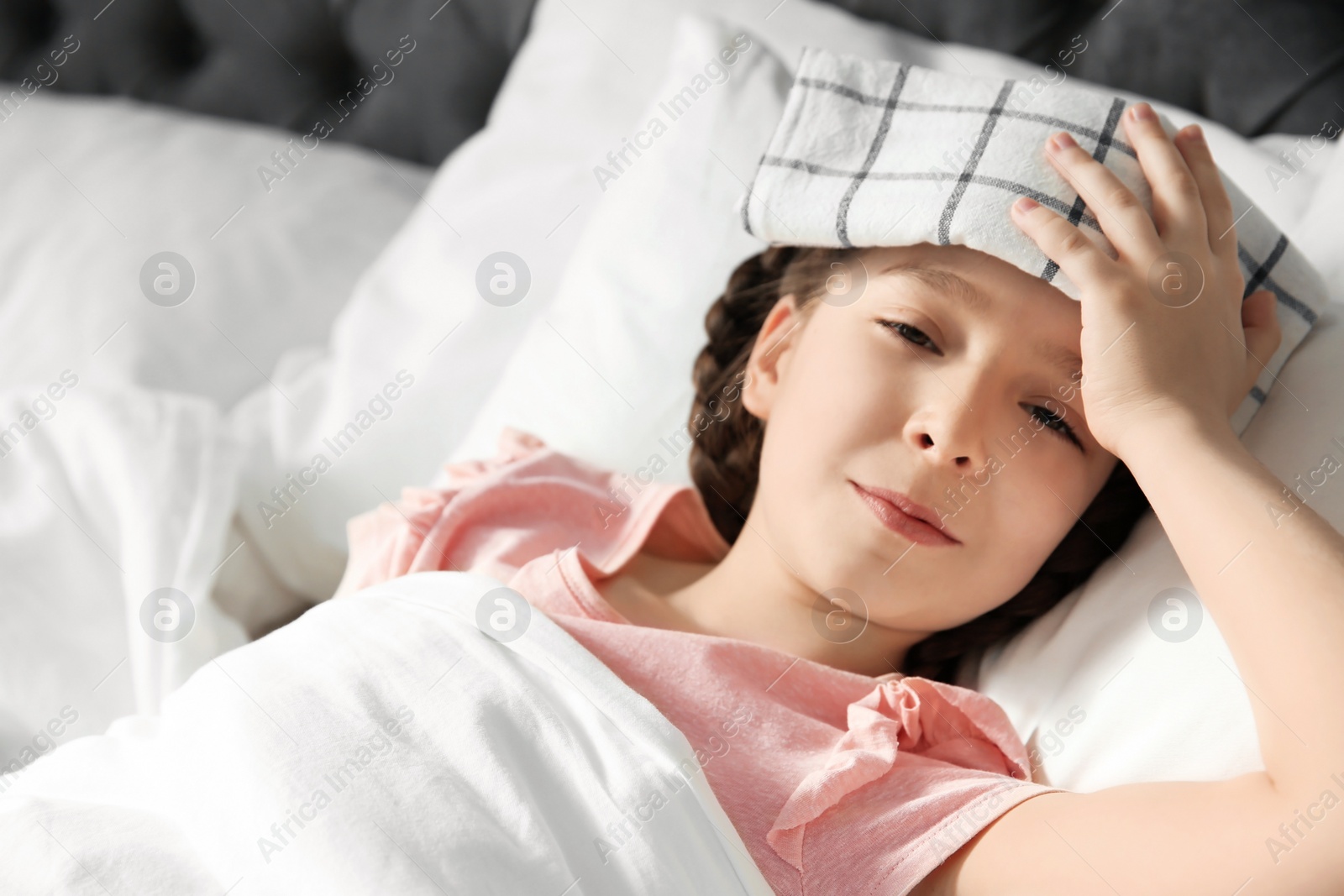 Photo of Little girl suffering from headache while lying in bed at home