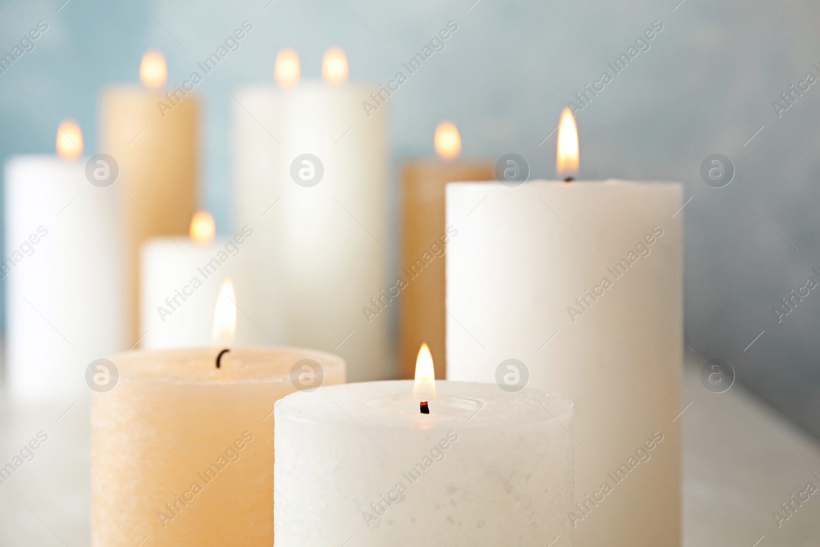 Photo of Burning candles on table against color background, closeup