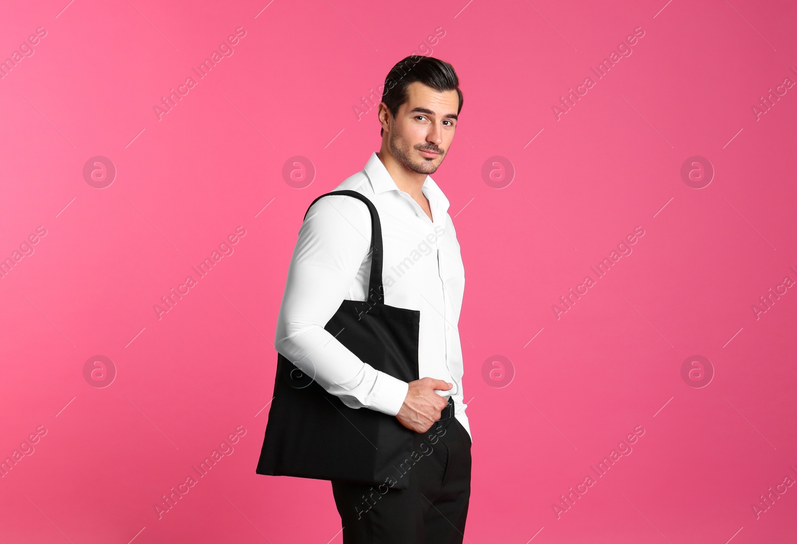 Photo of Young handsome man holding black tote bag on pink background, space for text