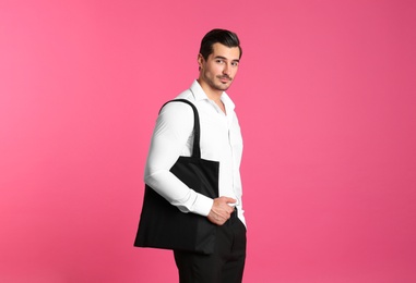 Young handsome man holding black tote bag on pink background, space for text