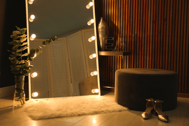 Photo of Stylish large mirror with light bulbs in dark room. Modern interior design