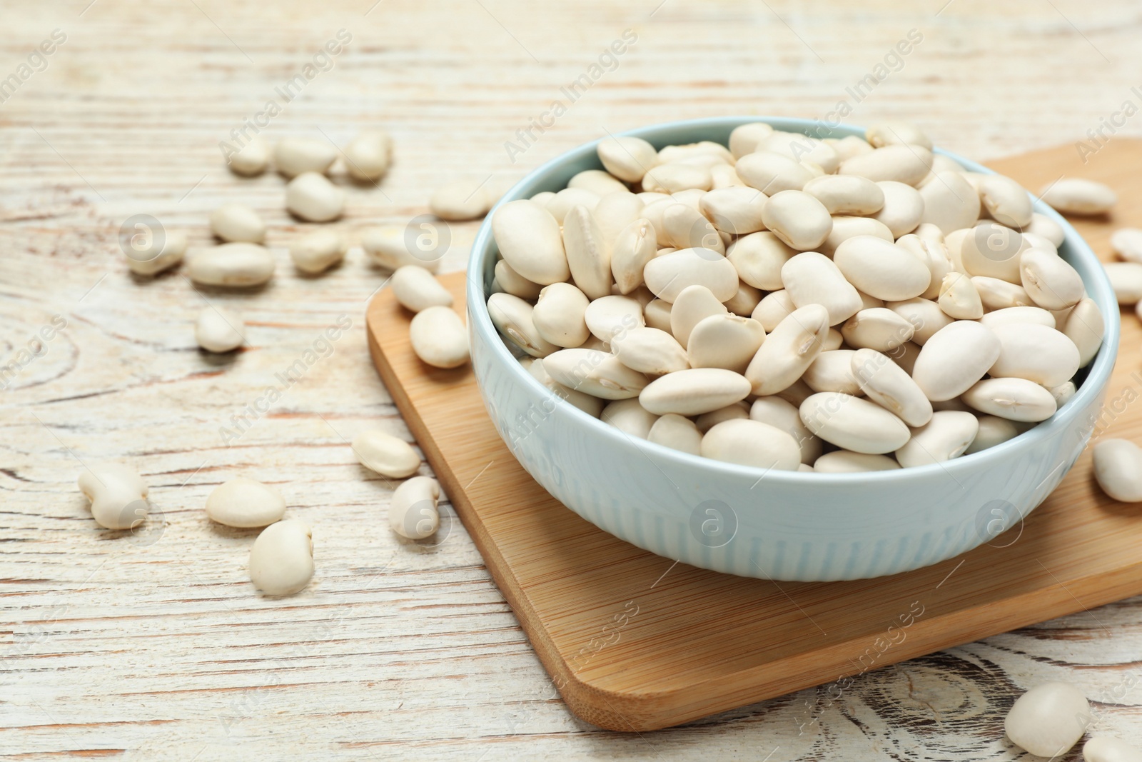 Photo of Bowl with uncooked white beans on wooden table
