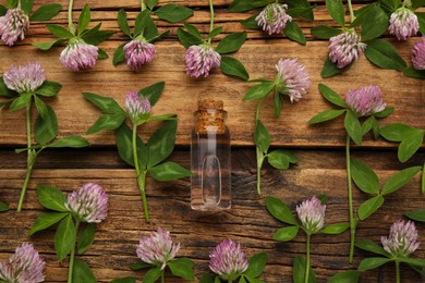 Beautiful clover flowers and bottle of essential oil on wooden table, flat lay