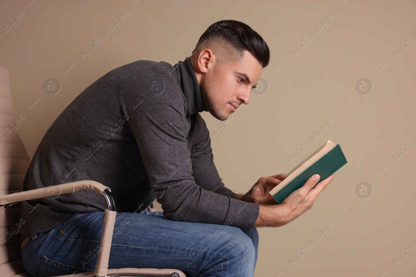 Photo of Man with poor posture reading book while sitting on chair against beige background
