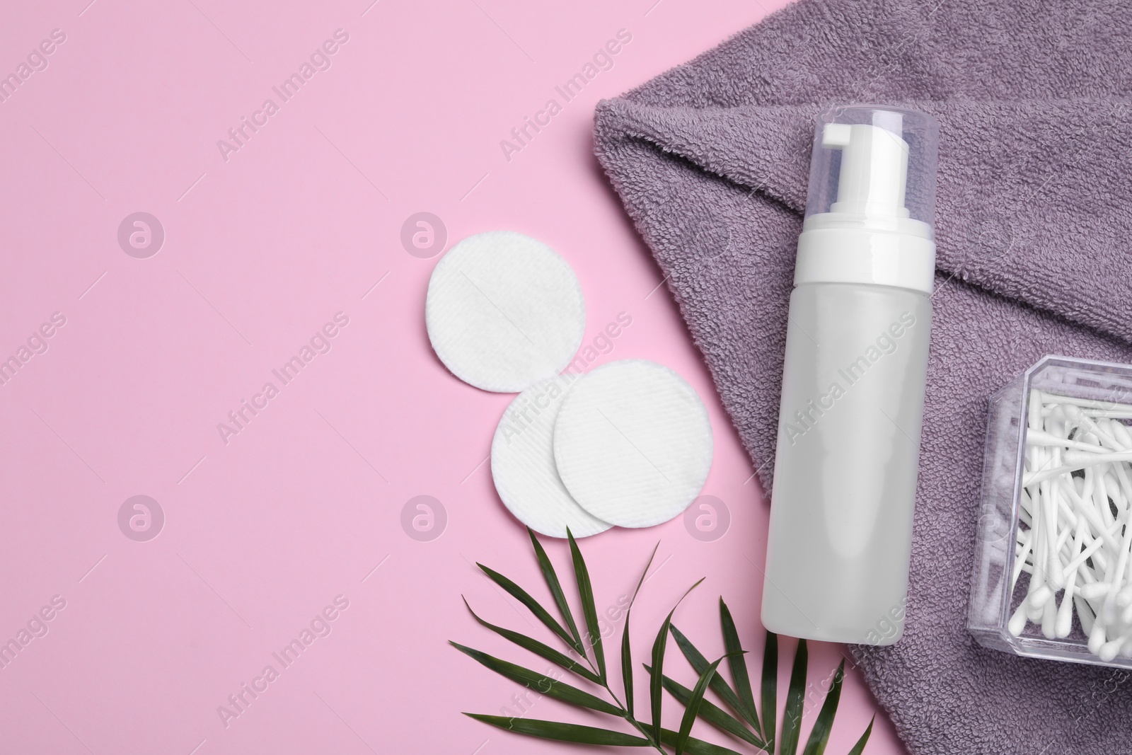 Photo of Bottle of face cleansing product, towel, cotton buds and pads on pink background, flat lay. Space for text