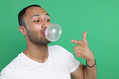 Photo of Man blowing bubble gum on green background. Space for text