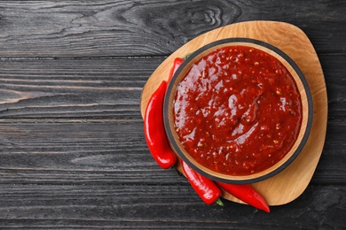Photo of Bowl of hot chili sauce with red peppers on dark wooden background, top view. Space for text