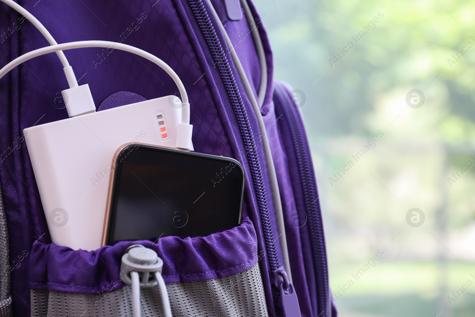 Photo of Charging mobile phone with power bank in purple backpack, closeup