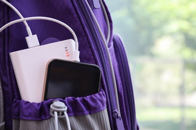 Photo of Charging mobile phone with power bank in purple backpack, closeup