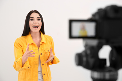 Young blogger recording video on camera against white background