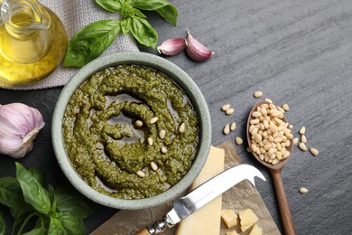 Photo of Tasty pesto sauce in bowl, basil, pine nuts, cheese, garlic and oil on black table, flat lay