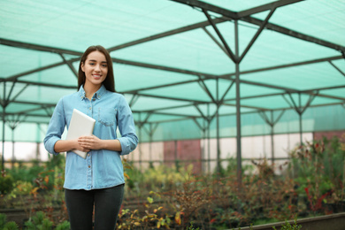 Female business owner with tablet in greenhouse. Space for text