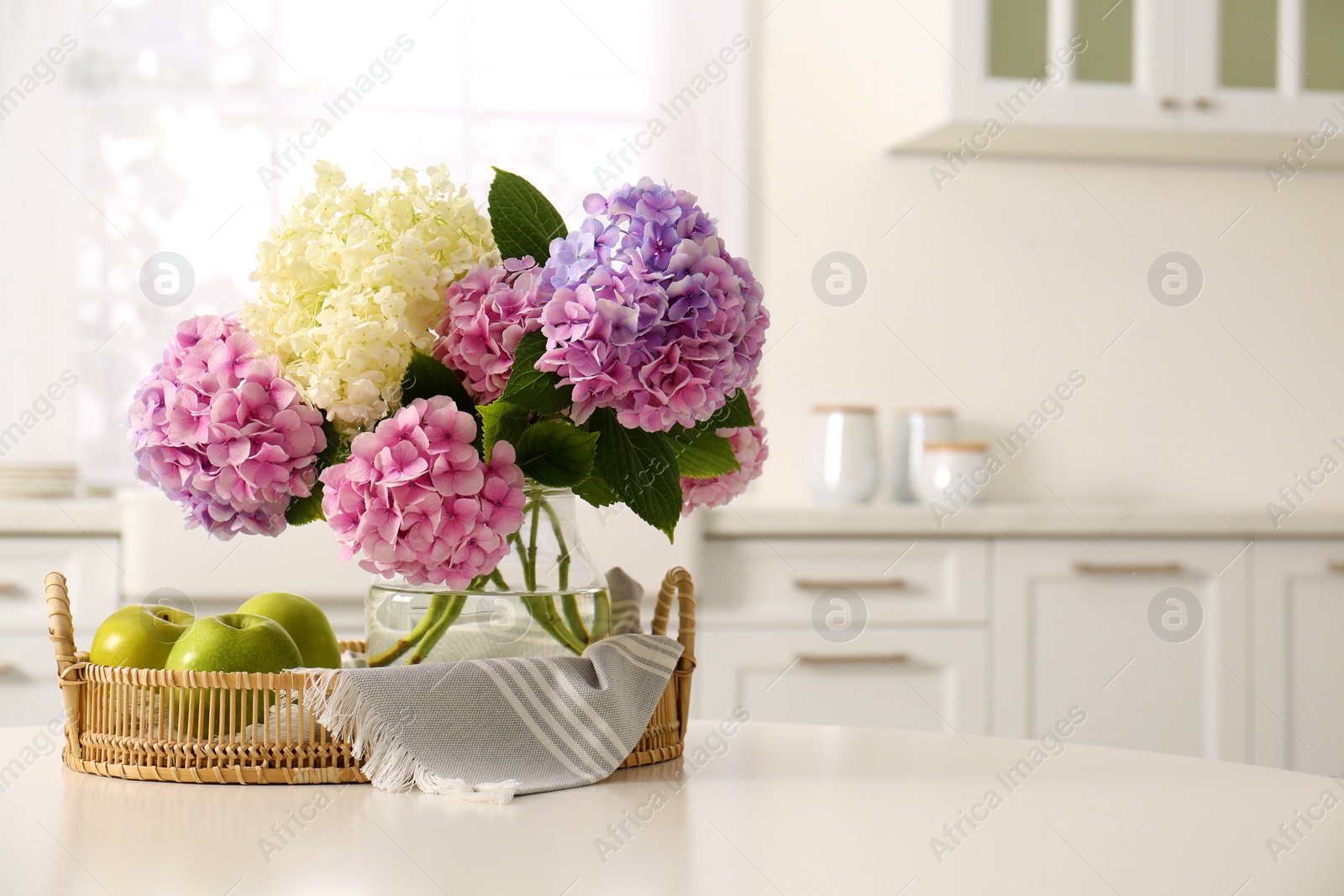 Photo of Bouquet of beautiful hydrangea flowers and apples on table in kitchen, space for text. Interior design