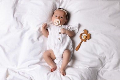 Photo of Cute little baby with pacifier and rattle lying on bed, top view