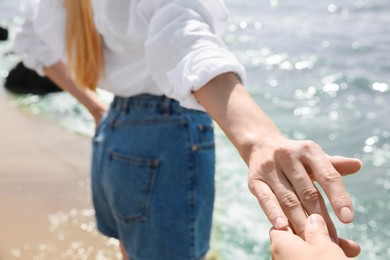 Young woman holding boyfriend's hand near sea on sunny day in summer