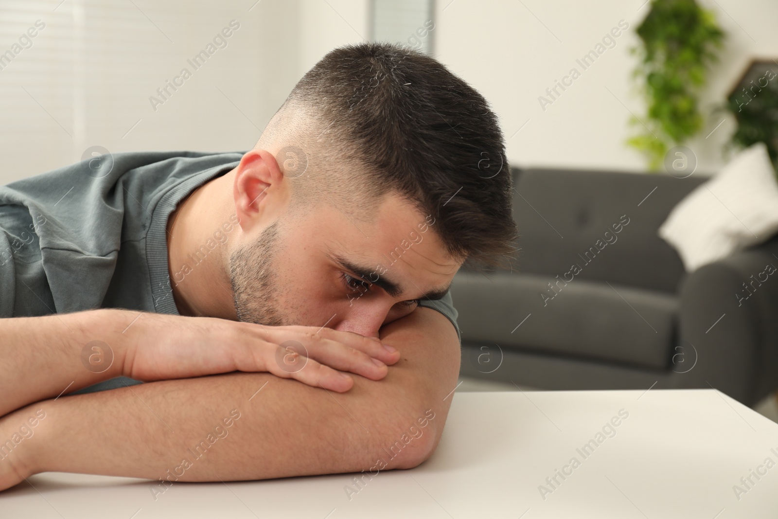 Photo of Sad man at white table indoors. Space for text