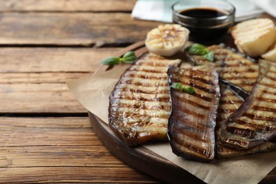 Photo of Delicious grilled eggplant slices served on wooden table, closeup