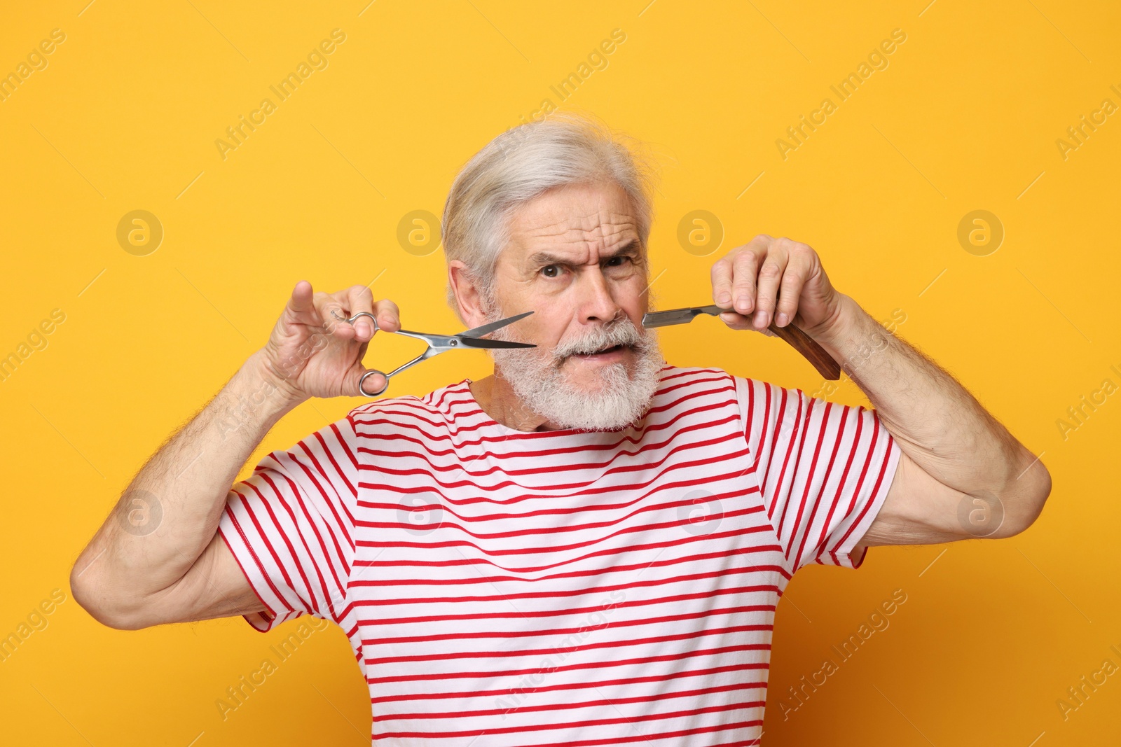 Photo of Senior man with mustache holding scissors and blade on orange background