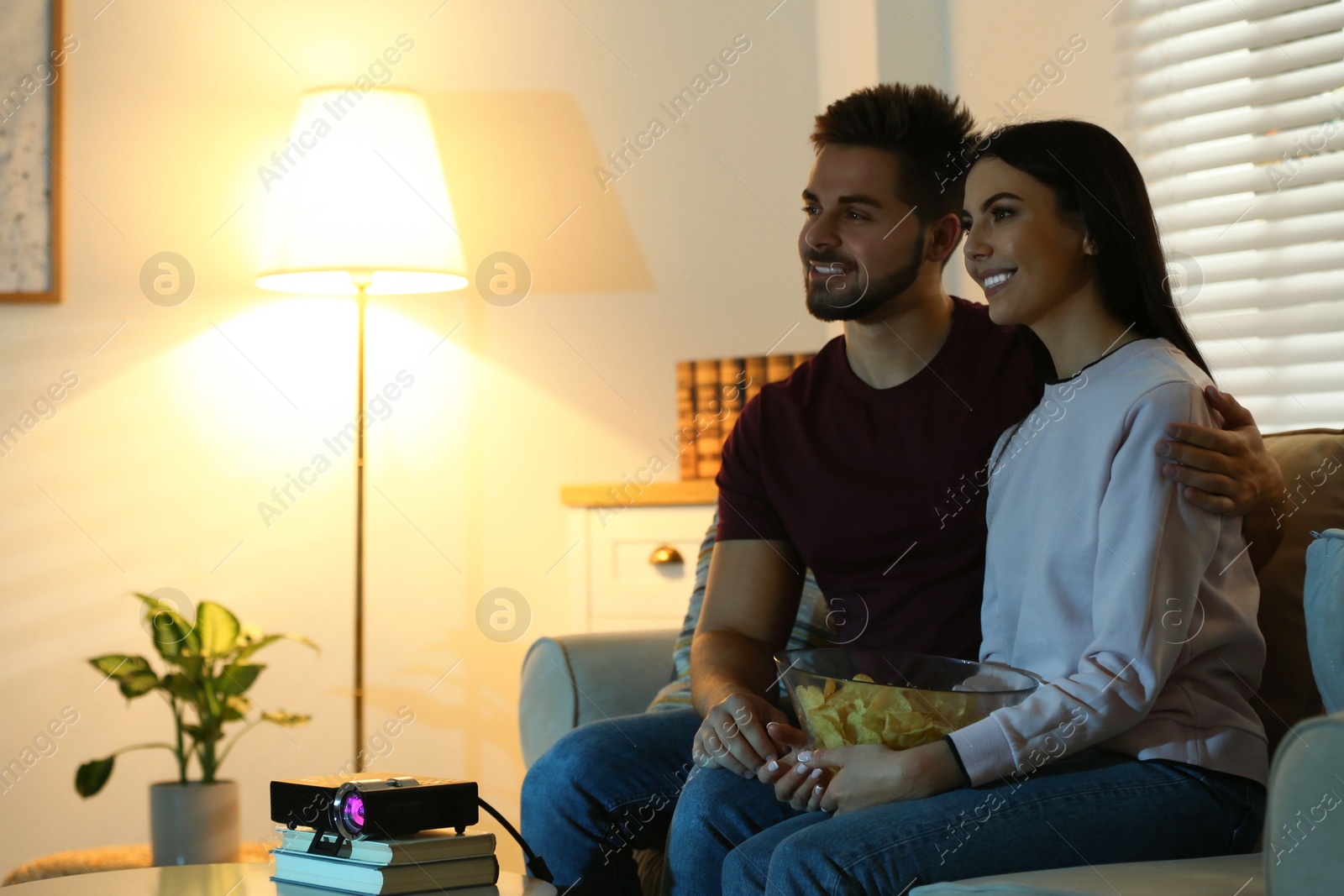 Photo of Young couple watching movie using video projector at home. Space for text