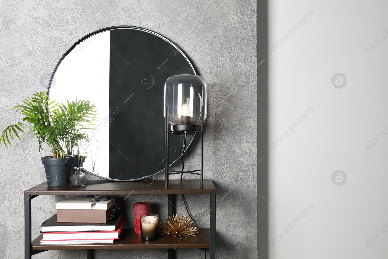 Photo of Stylish round mirror, lamp and houseplant on stand indoors. Interior design