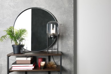 Photo of Stylish round mirror, lamp and houseplant on stand indoors. Interior design