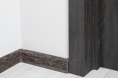 Black wooden plinth with connector on laminated floor near door indoors