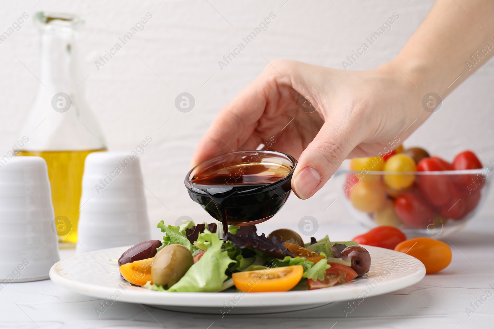 Photo of Woman pouring tasty vinegar into plate with salad at light table, closeup