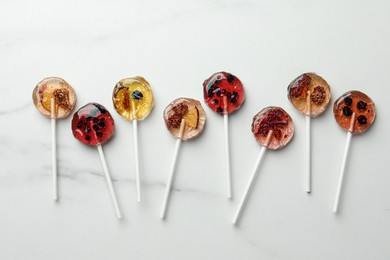 Photo of Sweet colorful lollipops with berries on white marble table, flat lay