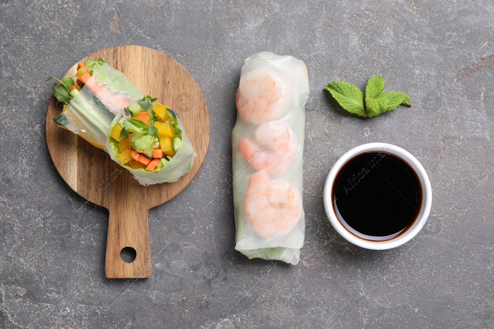 Photo of Tasty spring rolls, mint and soy sauce on grey textured table, flat lay