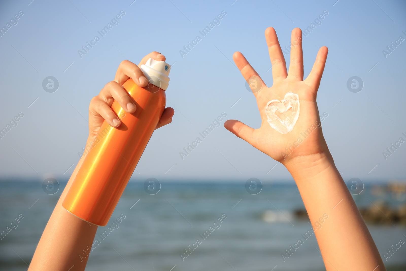 Photo of Child with bottle of sunscreen near sea, closeup. Sun protection care