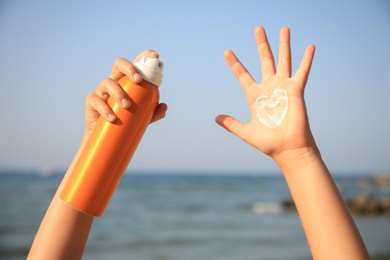 Photo of Child with bottle of sunscreen near sea, closeup. Sun protection care