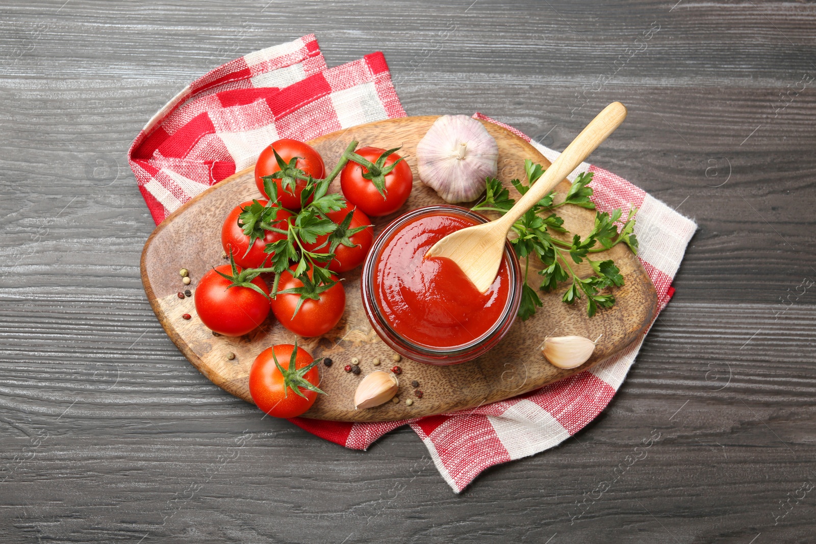 Photo of Tasty ketchup, fresh tomatoes, parsley and spices on grey wooden table, flat lay