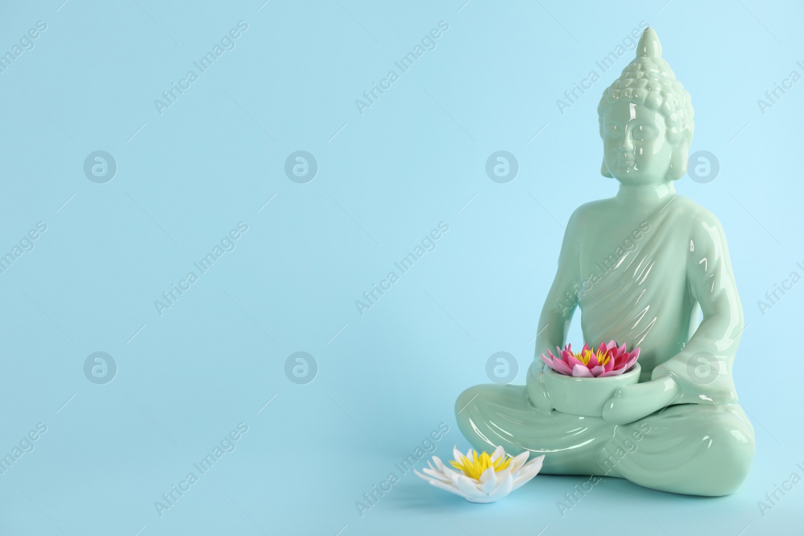 Photo of Beautiful ceramic Buddha sculpture with flowers on light blue background. Space for text