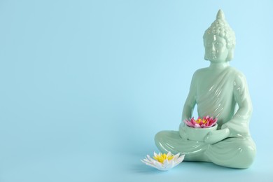 Photo of Beautiful ceramic Buddha sculpture with flowers on light blue background. Space for text