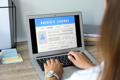 Photo of Woman using laptop to fill driver's license application form at table in office, closeup