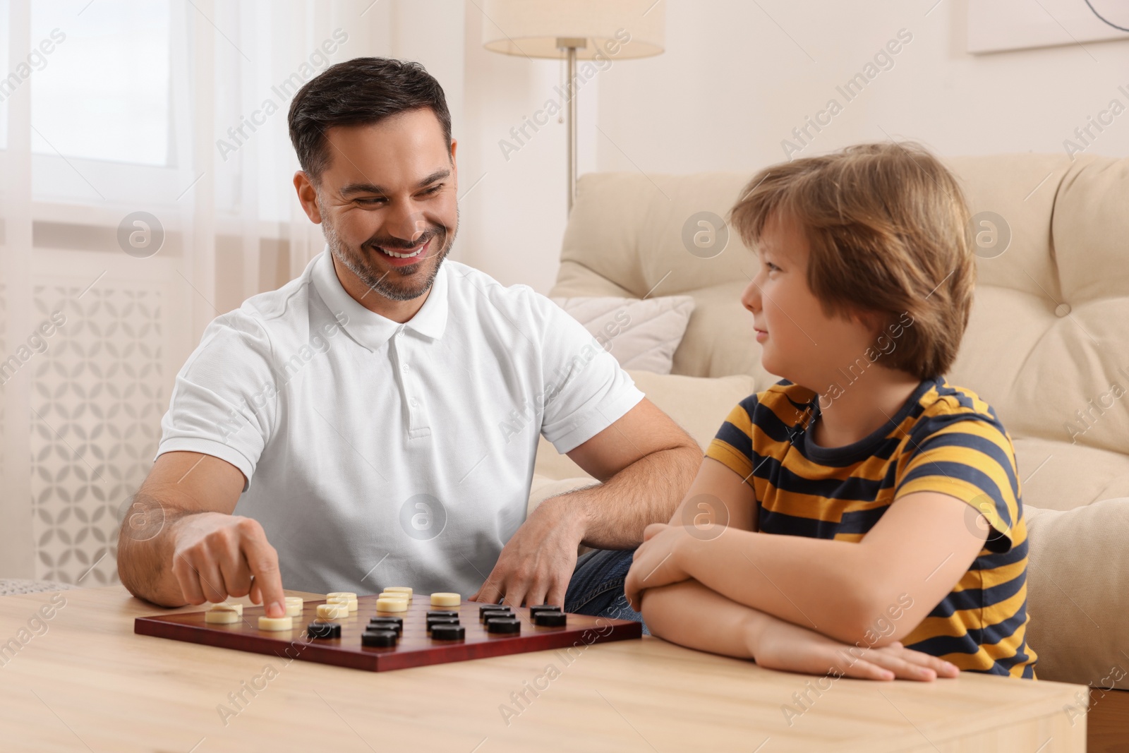 Photo of Father playing checkers with his son at table in room