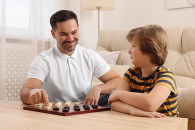 Photo of Father playing checkers with his son at table in room