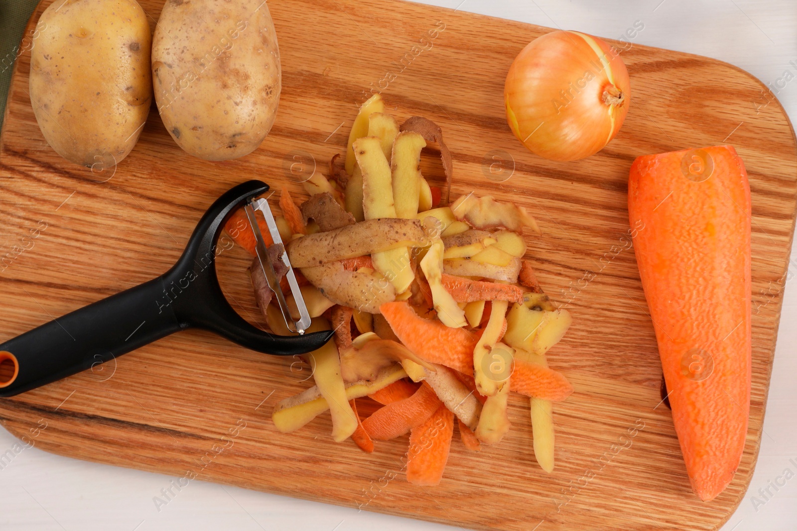 Photo of Peels of fresh vegetables and peeler on white table, top view