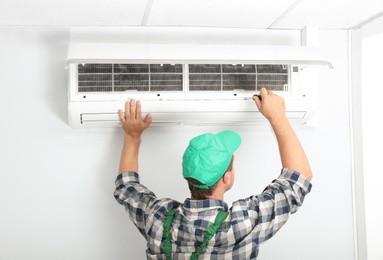 Photo of Male technician fixing modern air conditioner indoors