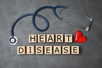 Photo of Wooden cubes with text Heart Disease and stethoscope on grey background, flat lay