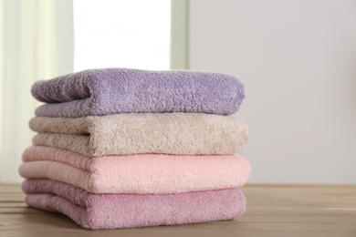 Photo of Stack of fresh towels on wooden table in bathroom, closeup