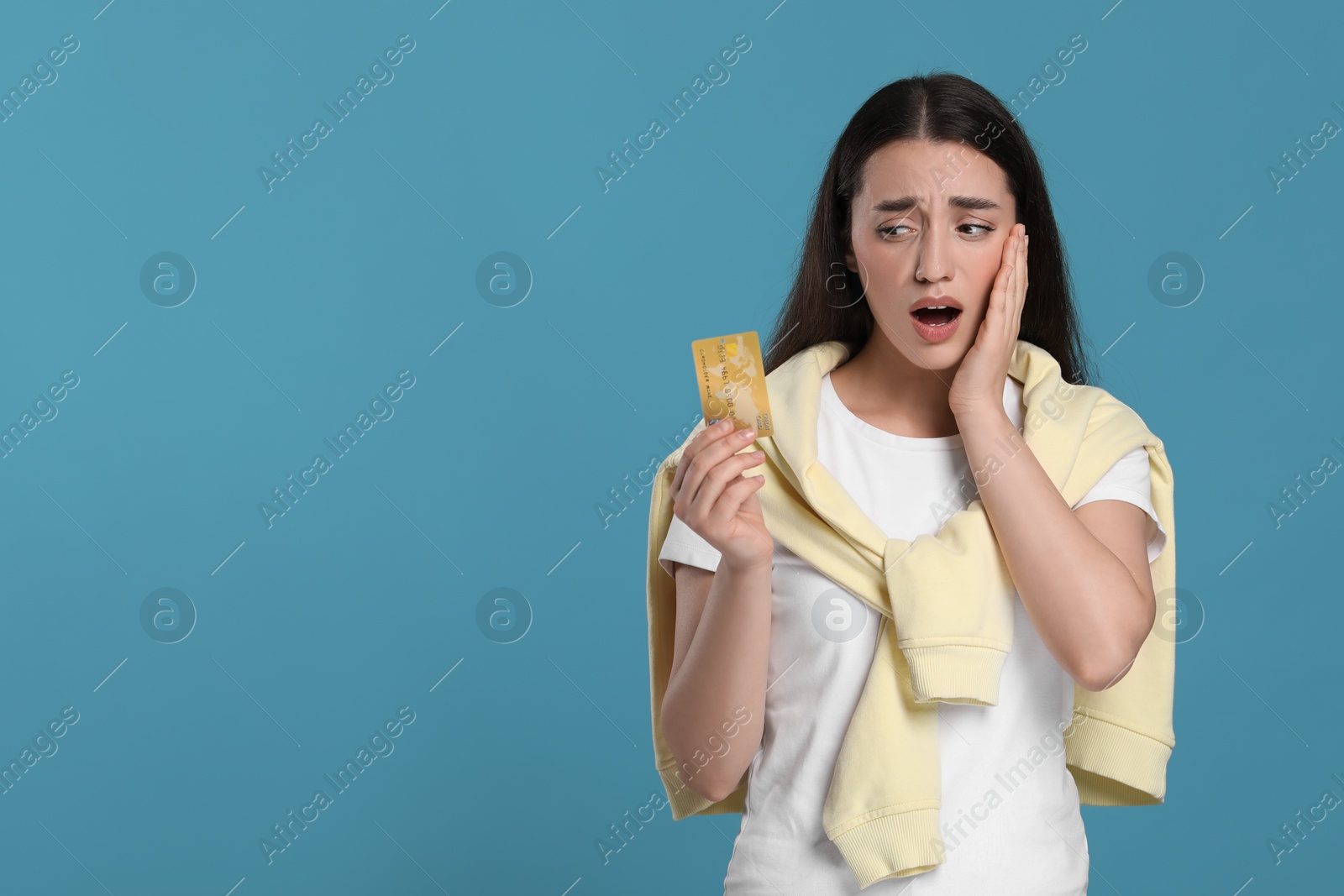 Photo of Shocked woman with credit card on light blue background, space for text. Debt problem