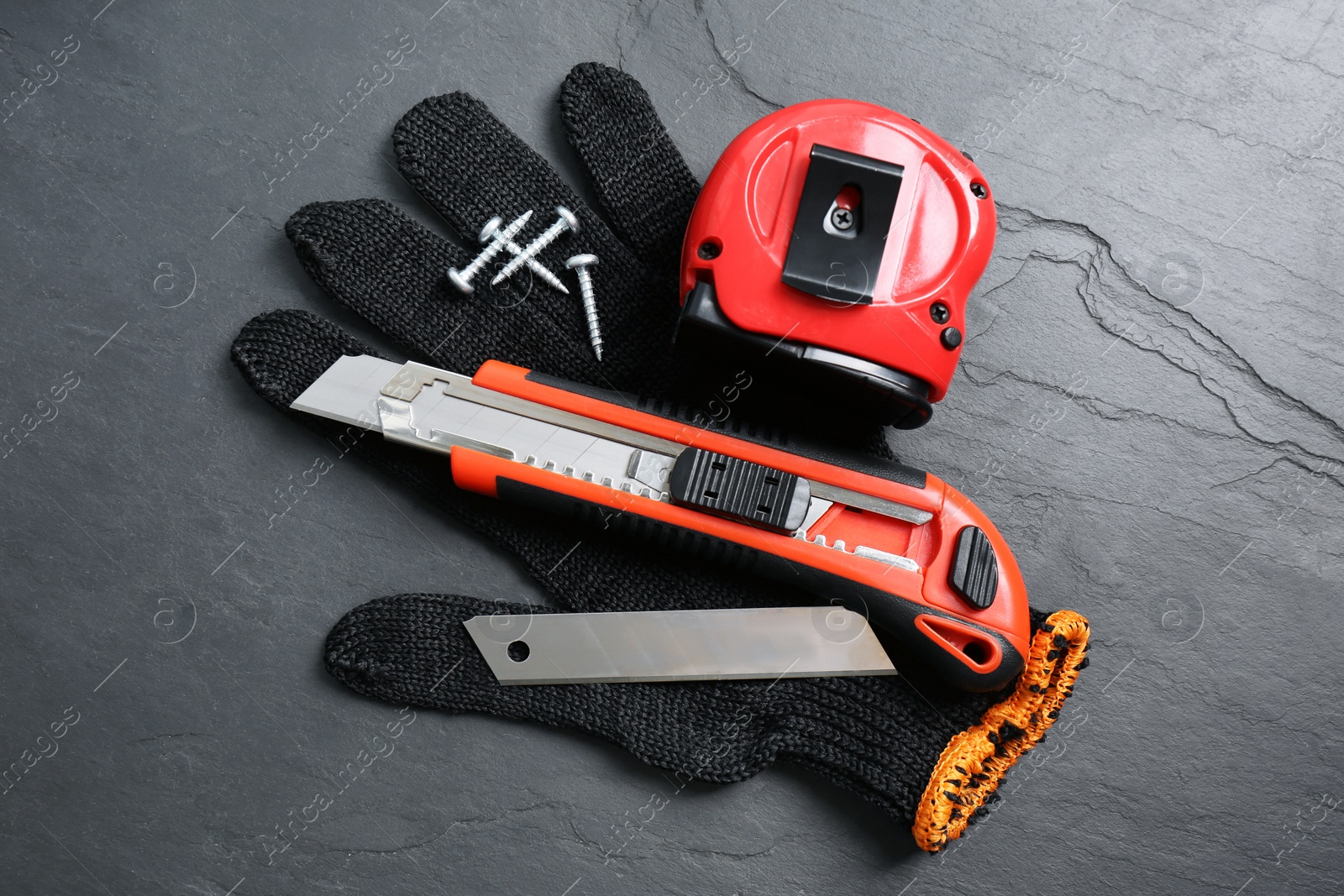 Photo of Utility knife, measuring tape and glove on black table, flat lay