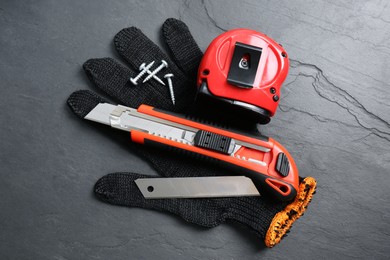 Photo of Utility knife, measuring tape and glove on black table, flat lay