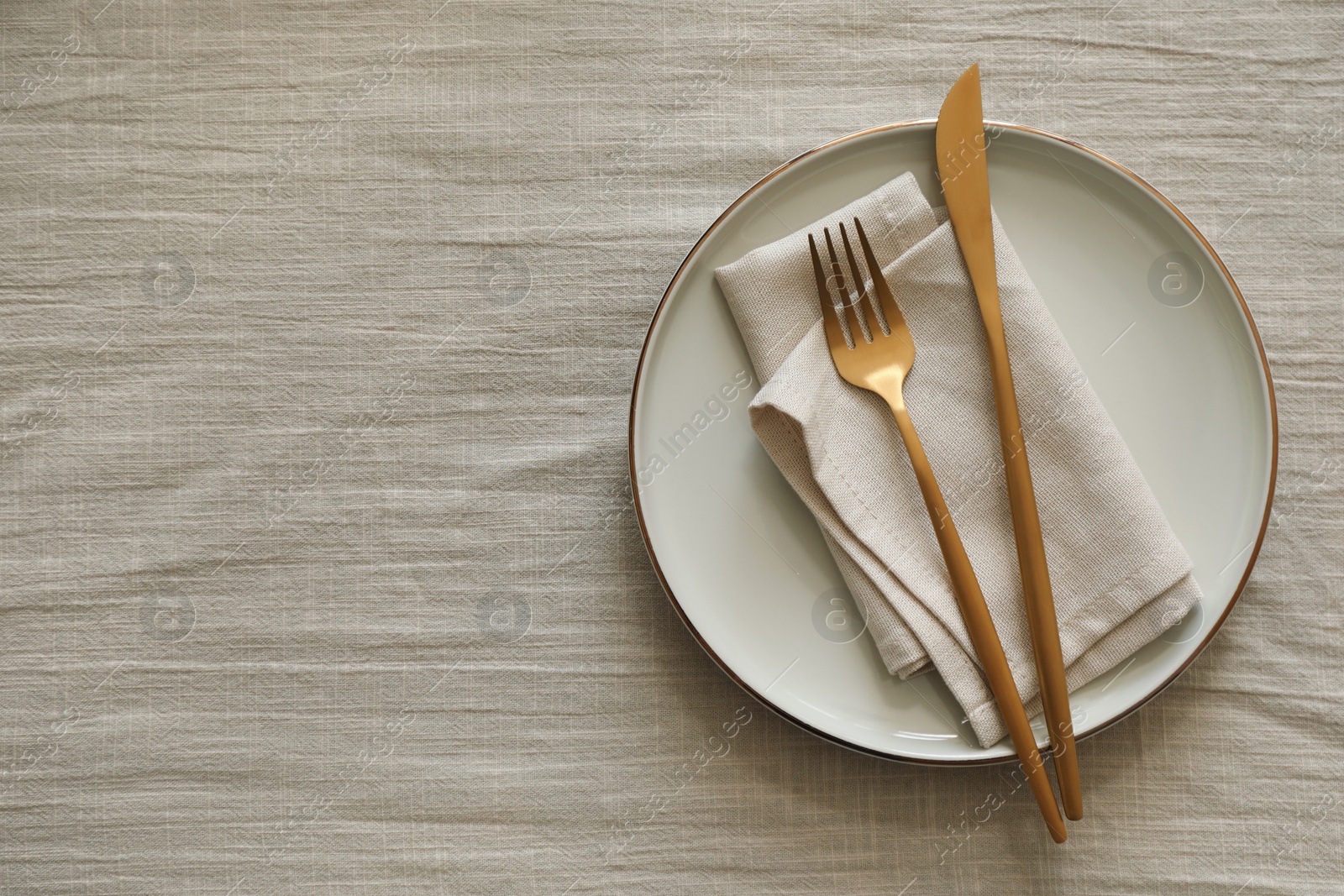 Photo of Stylish setting with cutlery, napkin and plate on light table, top view. Space for text