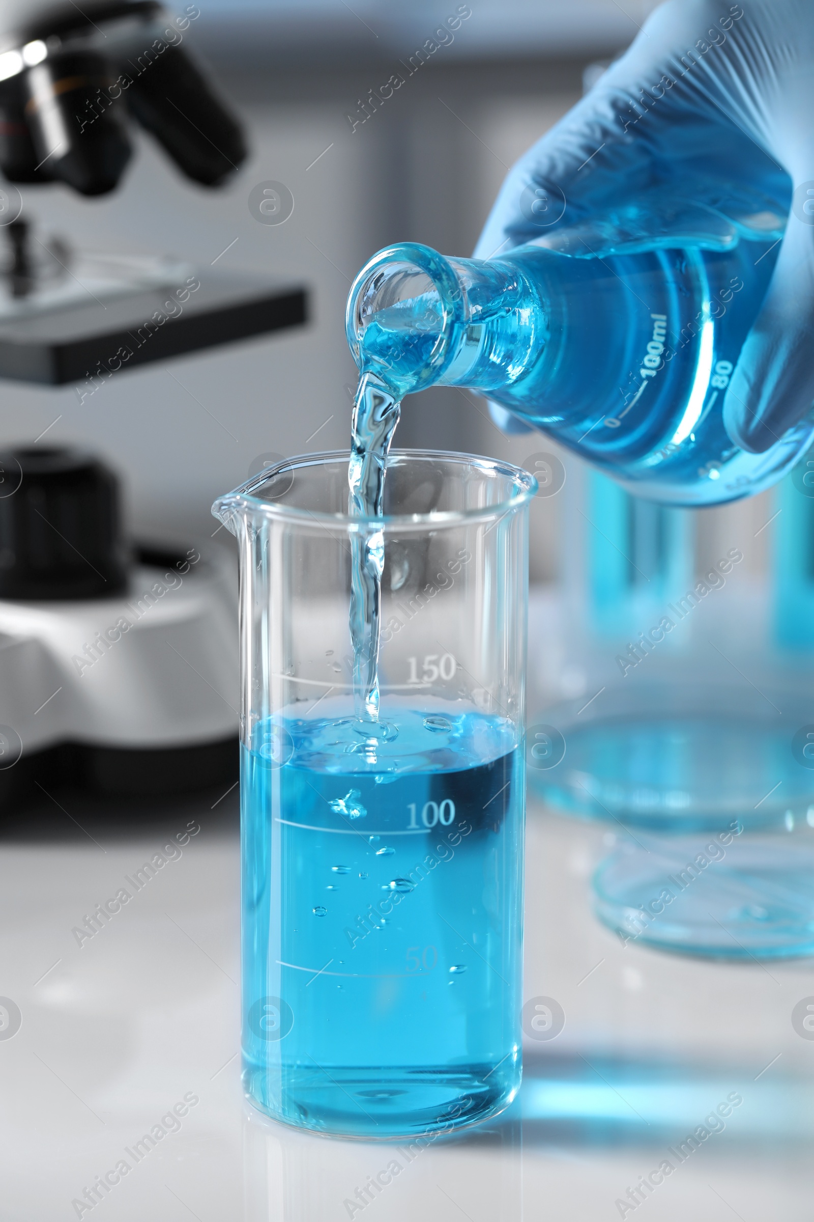 Photo of Scientist pouring light blue liquid from flask into beaker in laboratory, closeup