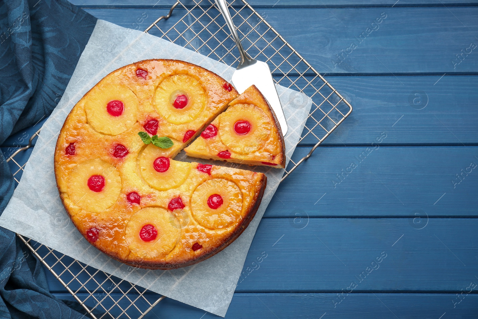 Photo of Delicious cut pineapple pie with cherry and mint on blue wooden table, top view. Space for text