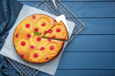 Delicious cut pineapple pie with cherry and mint on blue wooden table, top view. Space for text